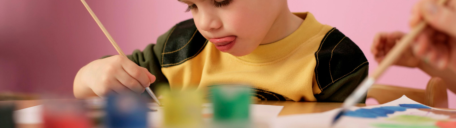 Les cours d'arts plastiques de l'académie de Nivelles illustrés par un petit garçon concentré sur son oeuvre, pinceau en main